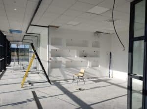 Chantier intérieur lumineux avec murs blancs, niches encastrées, échelle jaune et noire, sol en béton brut, et câbles pendant.