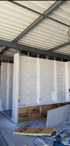 Chantier intérieur avec pose de plaques de plâtre sur ossature métallique, isolation ISOVER visible sous une ouverture.